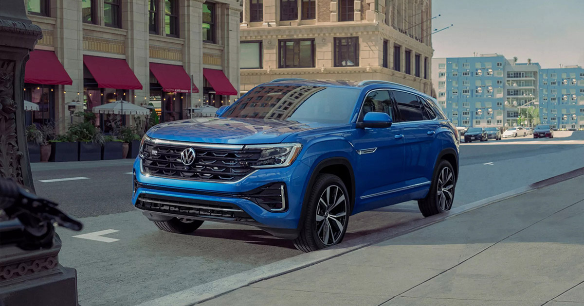 Blue 2024 Volkswagen Atlas Cross Sport SUV parked on urban street, sleek design with modern cityscape background