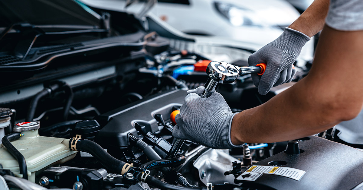 Auto mechanic using ratchet wrench to repair car engine, wearing protective gloves during vehicle maintenance service