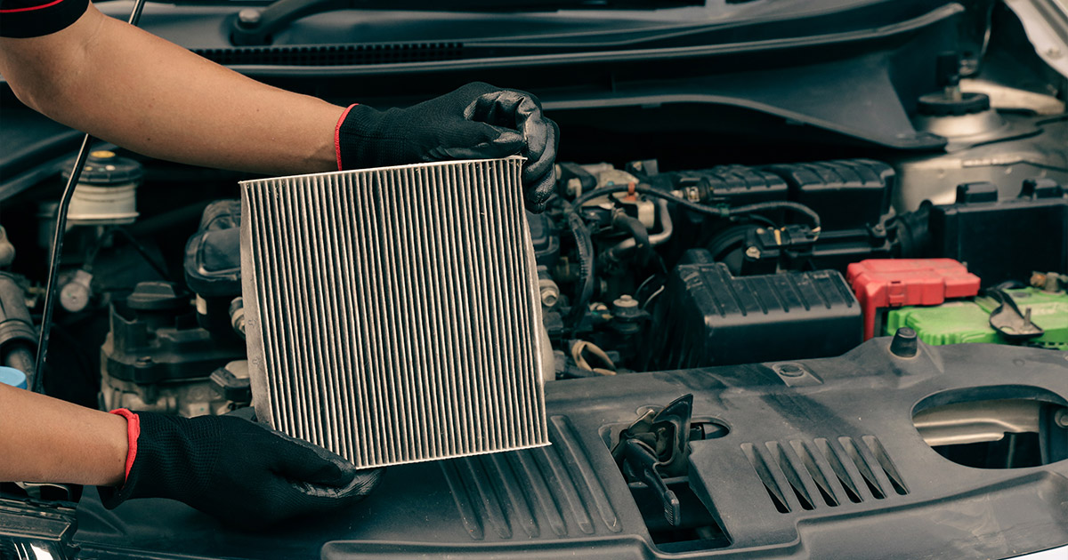Auto mechanic holding a clean cabin air filter during car maintenance, wearing black protective gloves
