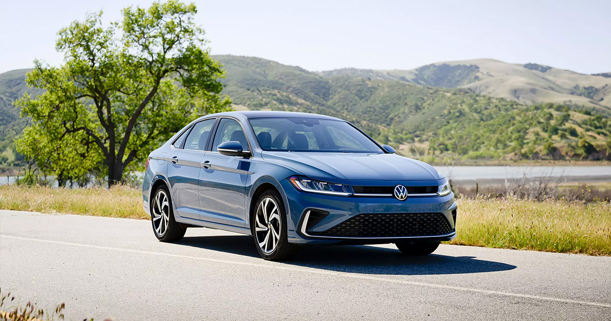 Blue Volkswagen Jetta sedan parked on rural road with mountains and tree in background, sleek modern design