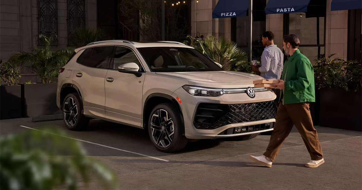 2025 Volkswagen Tiguan parked outside pizza restaurant, modern design with two people walking nearby at night