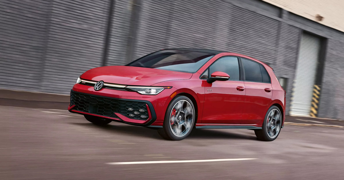 Red Volkswagen Golf GTI hatchback driving dynamically past industrial building with blurred motion