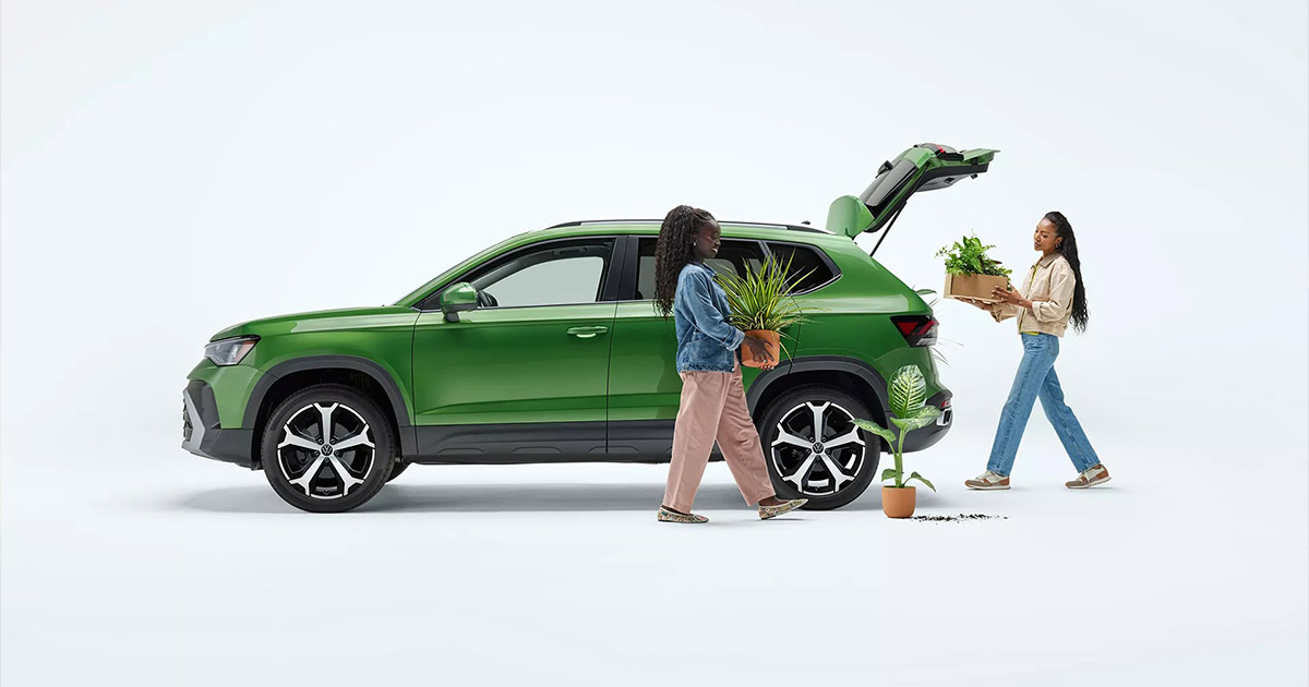 Green Volkswagen SUV with open trunk, two people loading plants, highlighting versatility and spaciousness